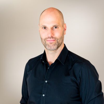 Portrait von Christof Schmid in schwarzem Hemd vor beigem Hintergrund